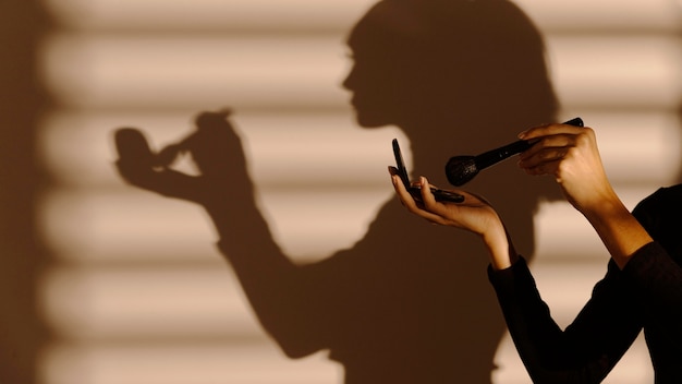 Free photo shadow of woman using different cosmetics