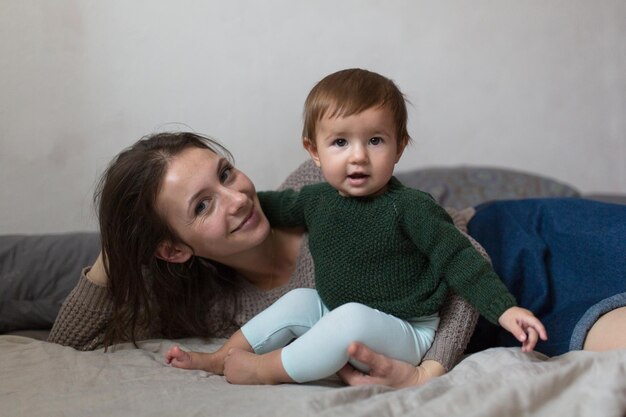 Shaggy young mother playing with baby on bed concept of comfort lifestyle