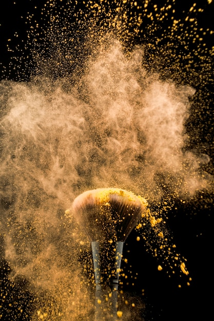 Free photo shaking cosmetic brush in yellow powder