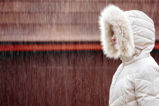 Messa a fuoco poco profonda di una femmina adulta che indossa un cappotto invernale bianco e cammina sotto la neve