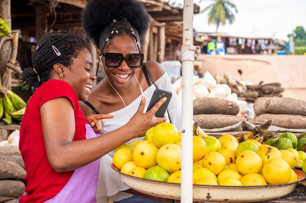 Shallow focus of an African female seller showing content in a phone to a customer at a market