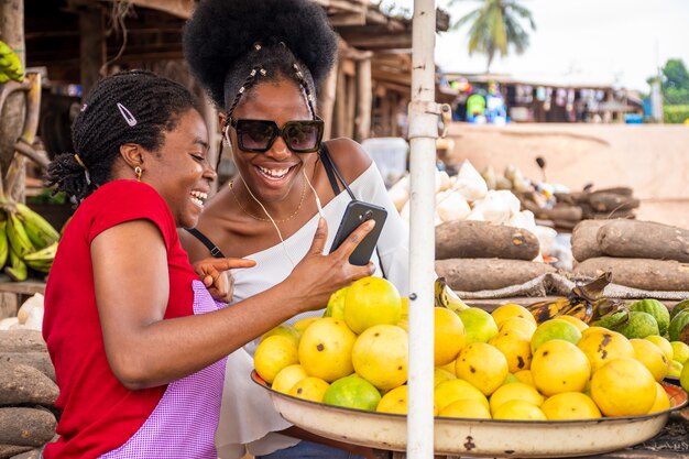 Shallow focus of an African female seller showing content in a phone to a customer at a market