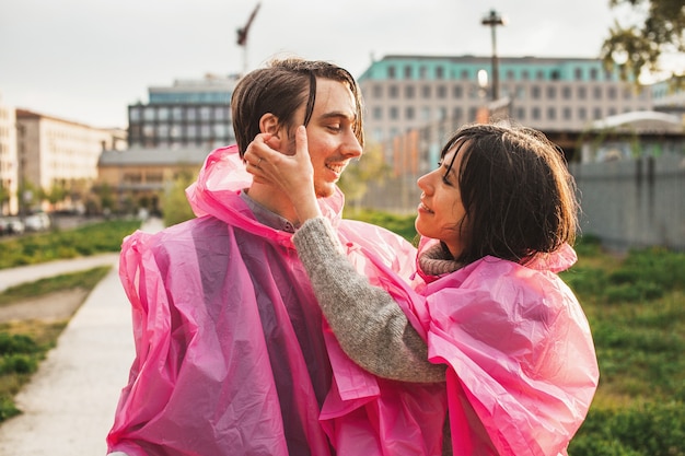 Shallow focus of a couple in pink plastic raincoats romantically looking at each other