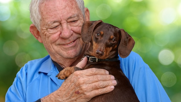 Free photo shallow focus of an elderly caucasian man holding an endearing dachshund dog