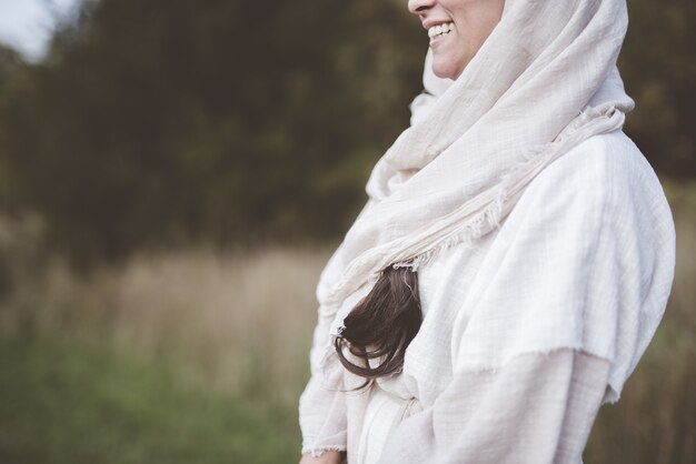 Shallow focus of a female wearing a biblical robe and smiling in a field