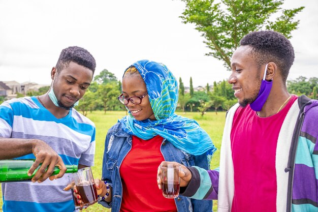 Shallow focus of a group of friends with facemasks pouring wine for each other in a park