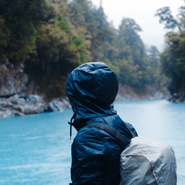 Shallow focus of a person wearing a raincoat with a backpack surrounded by trees during the rain