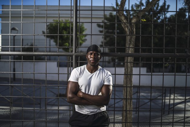 Shallow focus shot of an African-American male in a white shirt leaning on a fence with arms crossed