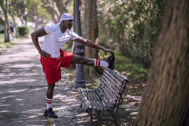 Shallow focus shot of an African-American male in a white shirt stretching on a bench at the park