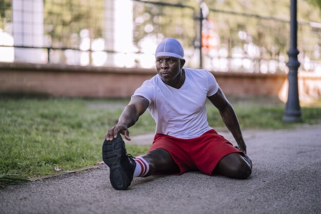 Shallow focus shot of an African-American male in a white shirt stretching at the park