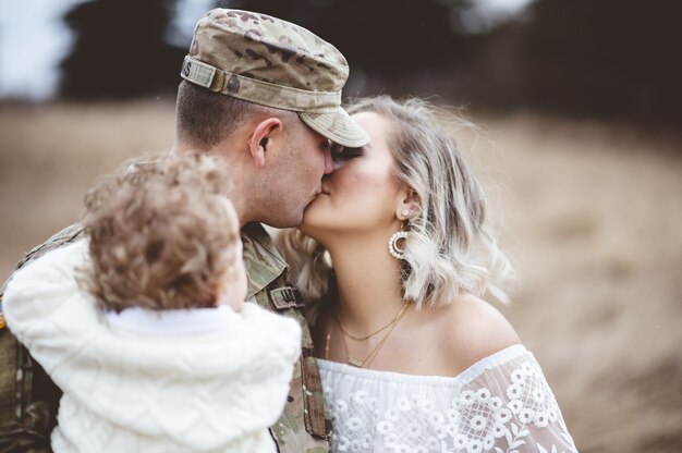 愛する妻にキスをしながら子供を運ぶアメリカ兵の浅いフォーカスショット