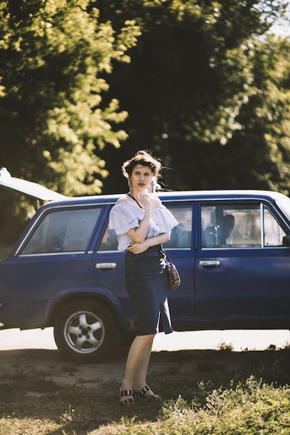 Shallow focus shot of an attractive female model in an off-shoulder dress posing near a vehicle