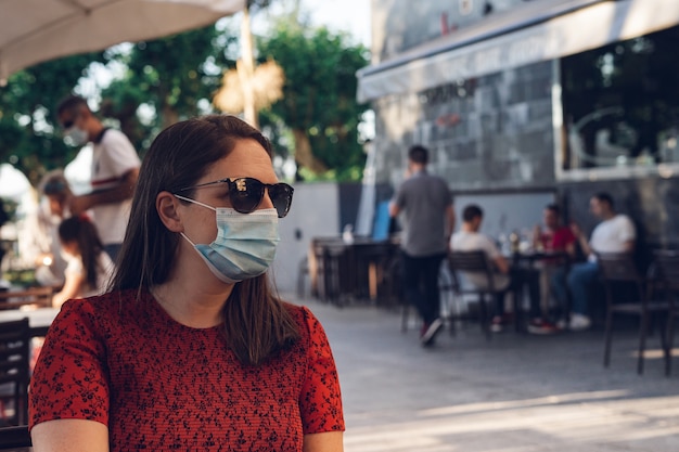 Free photo shallow focus shot of a caucasian female wearing a medical mask and sunglasses sitting in a cafe