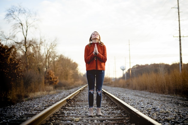 祈りながら電車の線路に立っている女性の浅いフォーカスショット