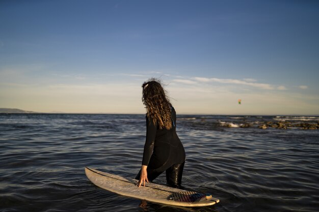 Неглубокий снимок женщины, идущей в море с доской для серфинга на боку