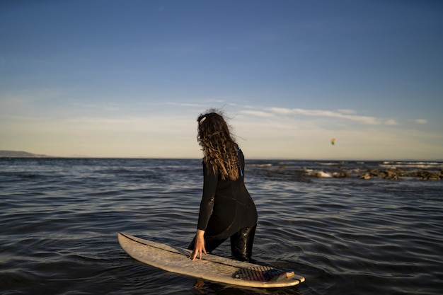 Shallow focus shot of a female walking in the sea with a surfboard on her side