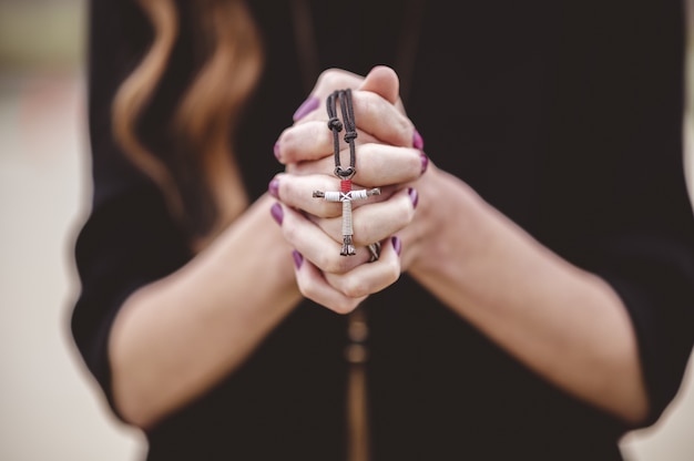 Shallow focus shot of a female wearing a black shirt while holding a cross in her hand