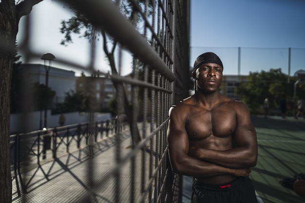 Foto gratuita shallow focus shot di un maschio afro-americano mezzo nudo appoggiato alla recinzione con le braccia incrociate