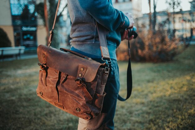 茶色の革のランドセルを身に着けてカメラを持っている男性の浅いフォーカスショット