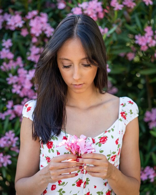 彼女の手にピンクの花を持つ若いブルネットの女性の浅いフォーカスショット