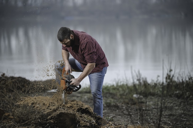 Free photo shallow focus shot of a young lumberjack cutting a tree with a chainsaw