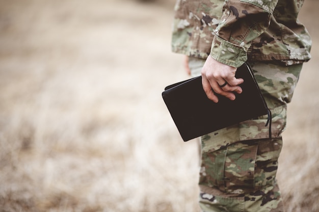 Free photo shallow focus shot of a young soldier holding a bible in a field