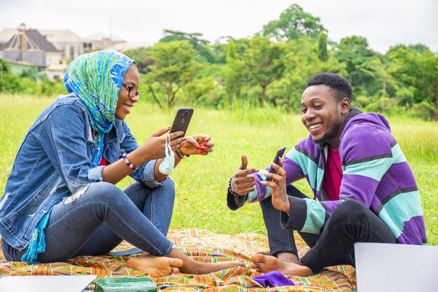 Shallow focus of two young friends hanging out at a park while using their phones