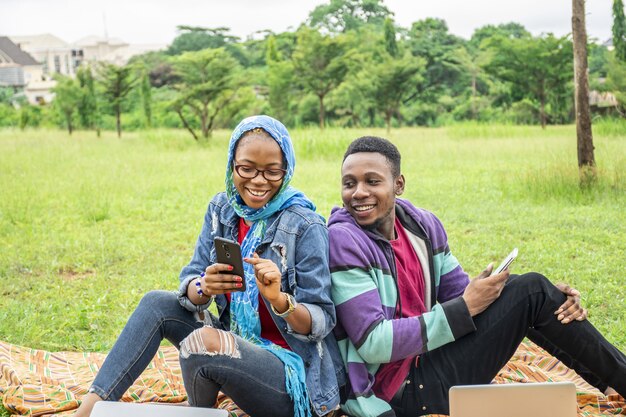 Shallow focus of two young friends hanging out at a park while using their phones