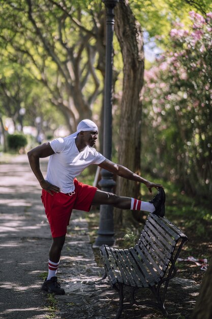 Shallow focus vertical shot of an African-American male in a white shirt stretching on a bench