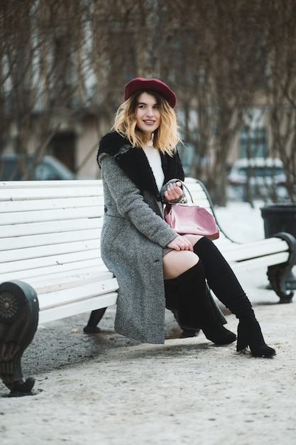 Shallow focus vertical shot of an attractive female in winter clothes sitting on a white bench