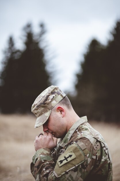 shallow focus vertical shot of a young soldier praying in a field