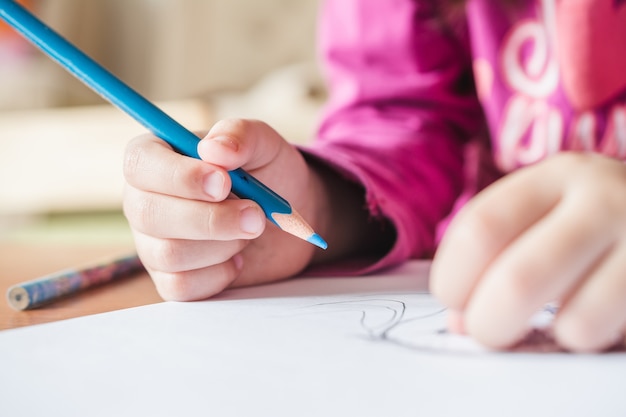 Неглубокий фокус на ребенка в розовой футболке, рисующего картину синим карандашом