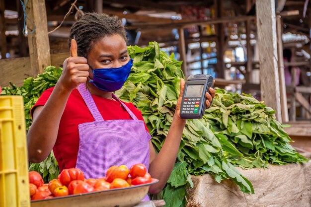 Shallow focus of an woman with a facemask holding a POS machine at a market