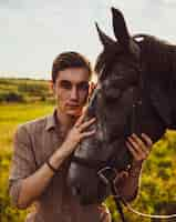 Free photo shallow focus of a young male petting a horse in a field under the sunlight