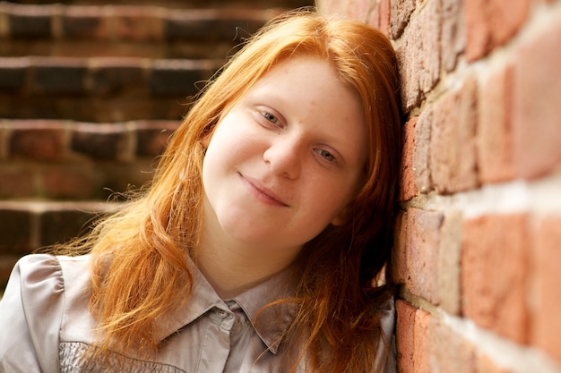 Shallow focus of a young red-haired female leaning on a brick wall