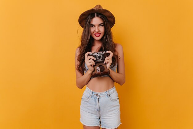 Shapely girl wears white shorts holding camera while standing on yellow space