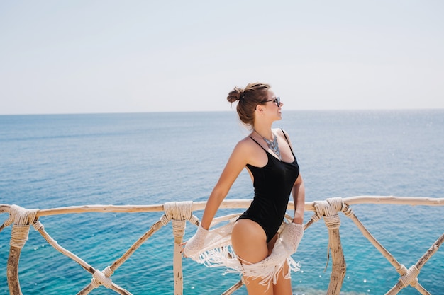 수평선을보고 바다에 서있는 유행 검은 수영복에 매끈한 우아한 소녀. 리조트에서 재미와 여름 아침에 바다 전망을 즐기는 아름 다운 젊은 여자의 초상화