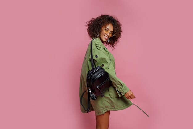 Shapely pretty woman with brown skin fooling around and posing in studio on pink background. Afro hairs.