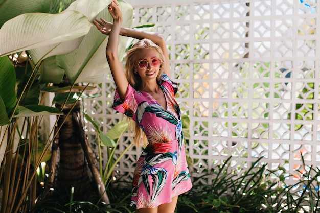 Shapely tanned girl posing with hands up on nature background and laughing.