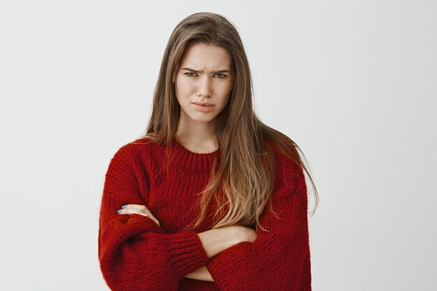 그녀는 그런 서투른 픽업 라인을 사지 않습니다. 빨간 느슨한 스웨터에 두 번 불쾌한 유럽 여성 학생, 손을 건너와 찡그림, 회색 벽에 불신과 좌절을 표현