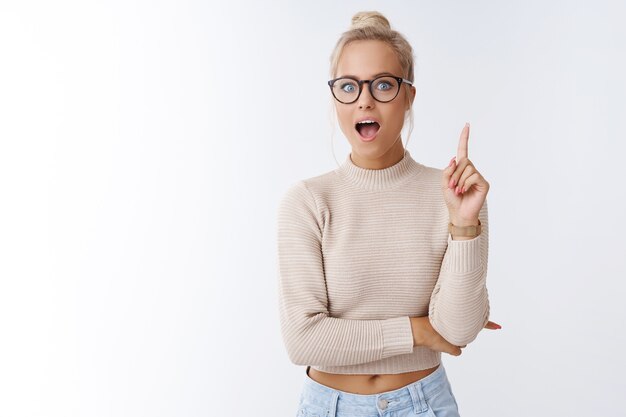 She got excellent idea. Indoor shot of enthusiastic creative young female designer adding suggestion raising index finger in eureka gesture open mouth to say plan posing over white background