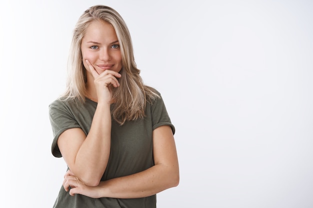 She knows key to success. Portrait of self-assured creative female sportswoman making plan smirking delighted and confident leaning face on fingers looking daring at camera over white background