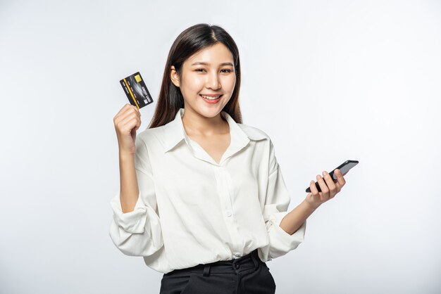 She was dressed in a white shirt and dark pants to go shopping and hold a credit card and smartphone