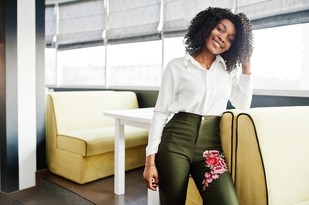 아프리카 머리를 한 순수한 비즈니스 아프리카계 미국인 여성은 카페에서 흰색 블라우스와 녹색 바지를 입고 포즈를 취했습니다.