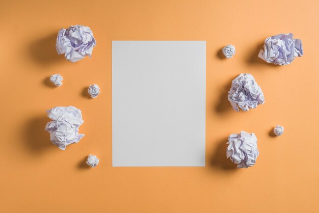 Sheet of white paper surrounded by crumpled papers over colorful backdrop