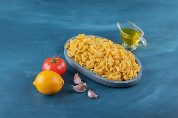 Shell uncooked pasta in a board on a dark-blue background.