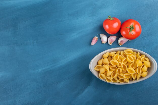 Shell uncooked pasta in a bowl with fresh red tomatoes and garlic . 