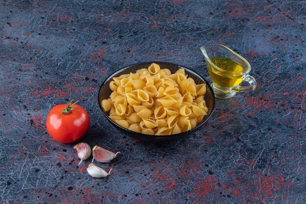 Shell uncooked pasta in a glass bowl with fresh red tomato and garlic . 