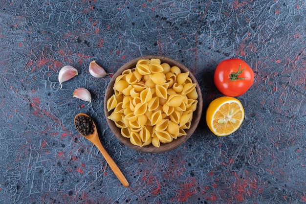 Shell uncooked pasta in a wooden bowl with fresh red tomato and sliced lemon . 