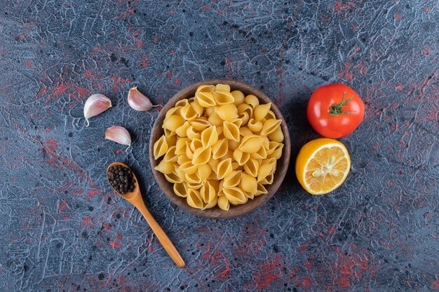 Shell uncooked pasta in a wooden bowl with fresh red tomato and sliced lemon . 